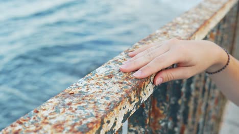 Woman-hand-gently-touching-eroded-handrail-on-Atlantic-ocean-coastline