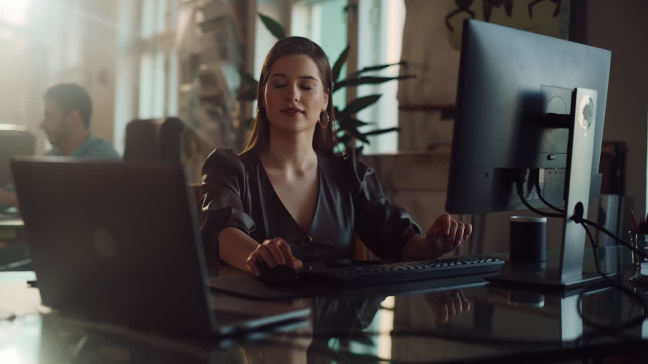 Two Stylish Employees Working on Computers in Creative Agency in Loft Office. Beautiful Manager Typing Correspondence Emails. Sunny Renovated Space with Plants, Artistic Posters and Rounded Windows.