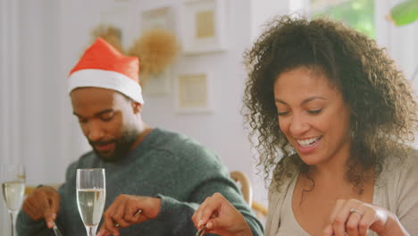 Familia-Multigeneracional-Con-Gorros-De-Papá-Noel-Disfrutando-De-Comer-Comida-Navideña-Juntos-En-Casa