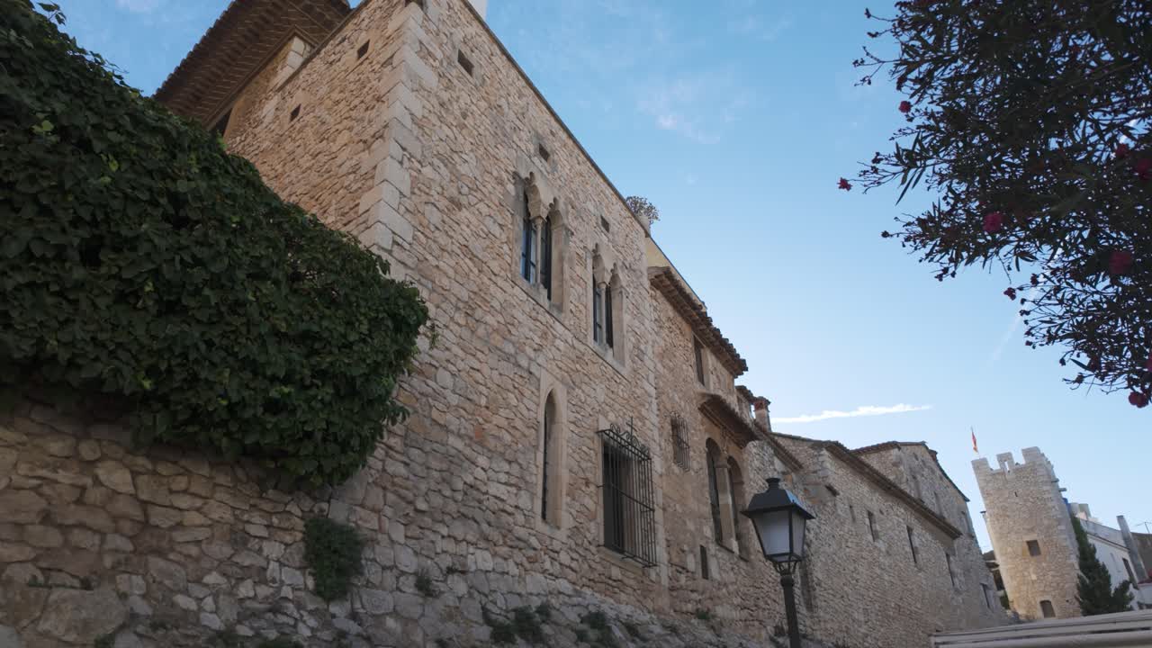 A historic stone building and ivy-covered wall in Sitges, Spain, under a bright sky