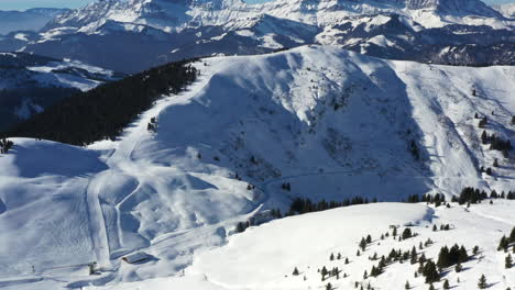 Aerial-shot-panning-up-to-show-Praz-sur-Arly-ski-resort,-and-a-mountain-skyline,-in-the-French-Alps-in-winter-with-sun-shine