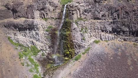 Aerial-dolly-shot-descends-down-small-waterfall-on-volcanic-rock-cliff