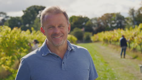 portrait of mature male owner of vineyard in field with workers at harvest