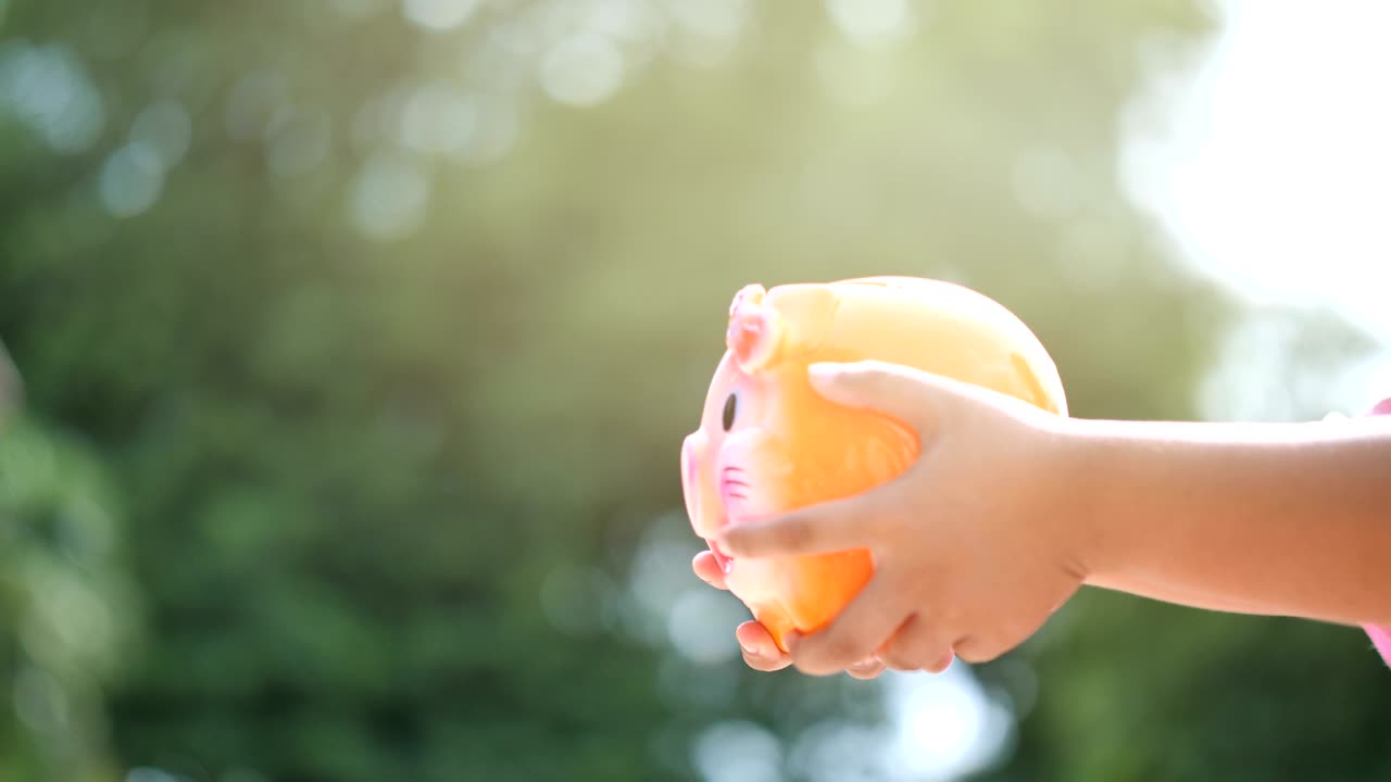돼지 은행을 들고 동전을 넣는 소년의 손, 느린 모션, 보케 배경, 돈을 저축하고 미래를 위해 돈을 모으는.