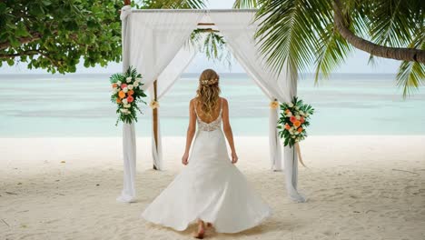 a beautiful bride approaches the beachside wedding arch, framed by lush greenery and floral arrangements, ready for a dreamy tropical ceremony on the shoreline