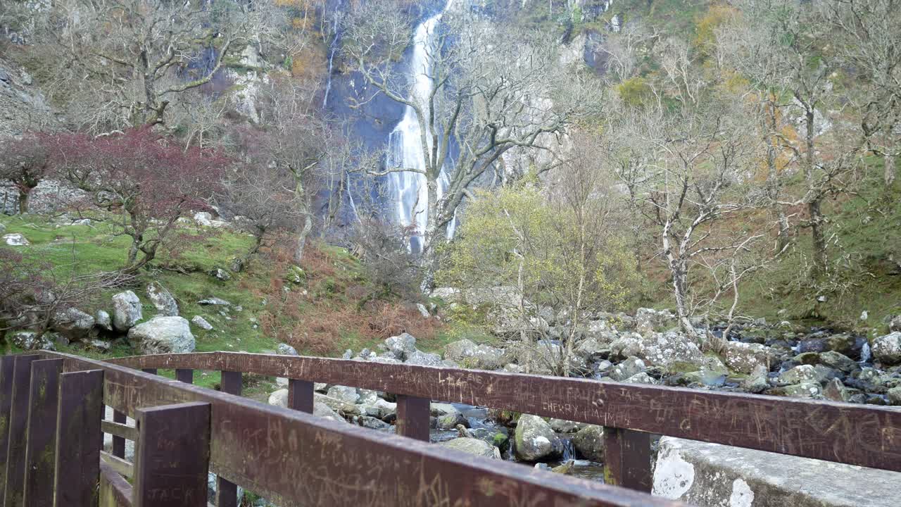 Cascata impetuosa, ponte di legno, scena autunnale con alberi spogli, carrellata a destra