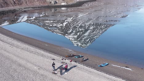 group of kayaking friends on shore of holmanes, reflection of hólmatindur mountain on flat water surface, aerial