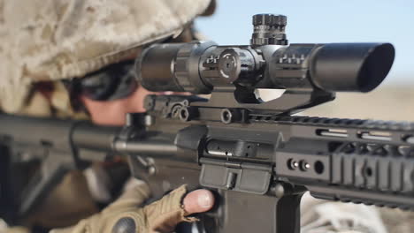 slow motion: a us marine positioned in the desert takes aim with his assault rifle while laying down and takes off the safety