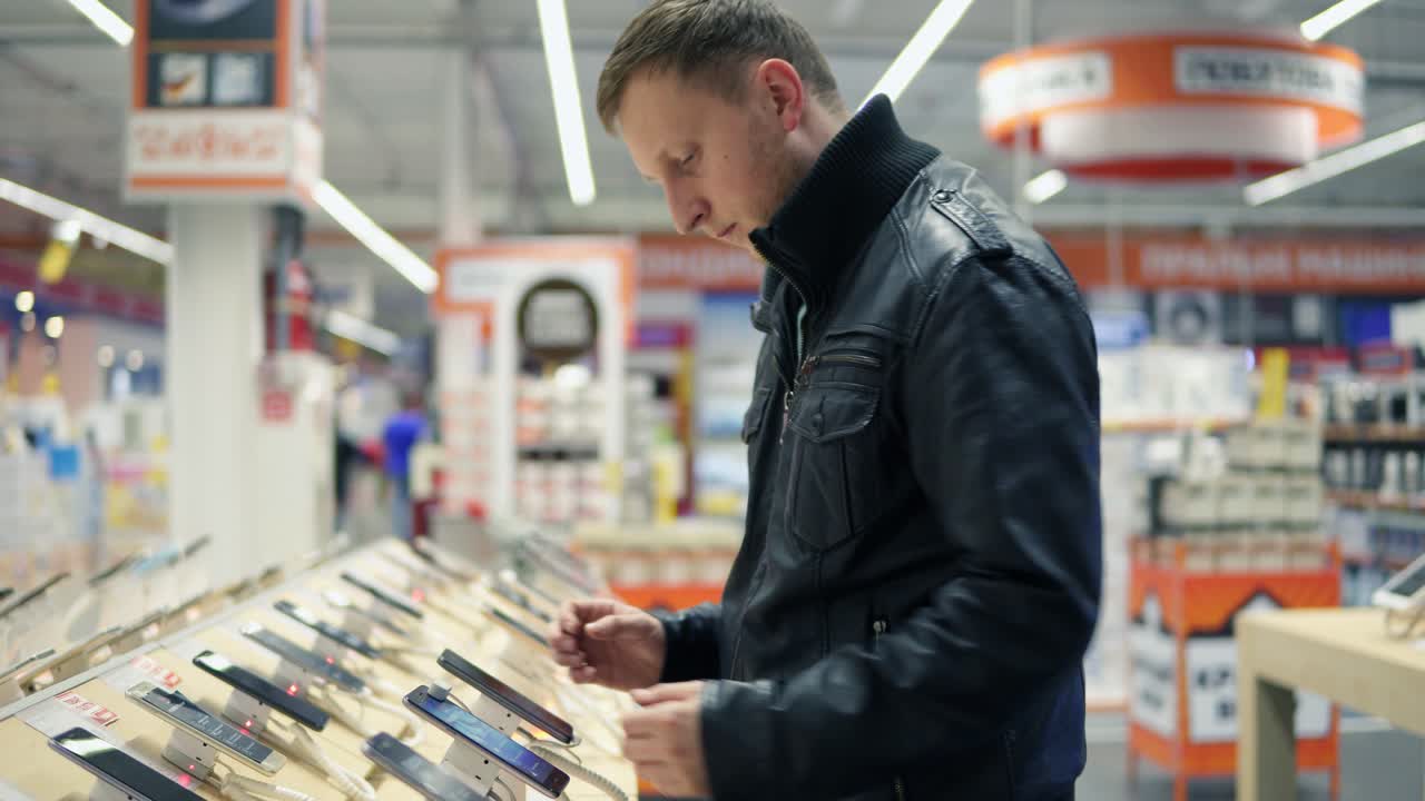 Young male customer choosing a new mobile phone in a shop, checking how it works