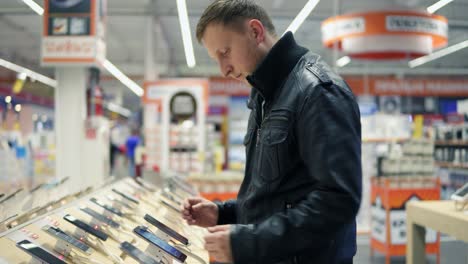 Young-male-customer-choosing-a-new-mobile-phone-in-a-shop,-checking-how-it-works