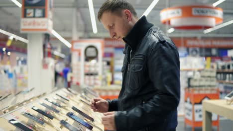 joven cliente masculino eligiendo un nuevo teléfono móvil en una tienda, comprobando cómo funciona