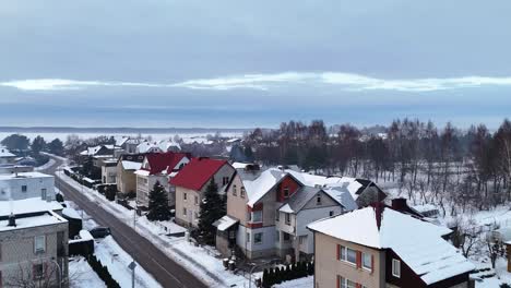 Drone-rises-above-snowy-roofs-in-suburban-neidhborhood-to-reveal-leafless-trees-and-white-landscape