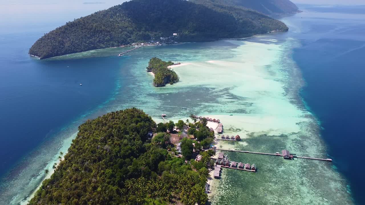 vista aérea panorámica de simples cabañas de playa con vistas a aguas cristalinas del océano con arrecifes de coral en el popular destino de buceo en raja ampat, papúa occidental, indonesia