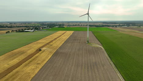 Vista-Aérea-De-Gran-Angular-De-Una-Turbina-Eólica-En-Campos-Agrícolas-Durante-La-Cosecha.