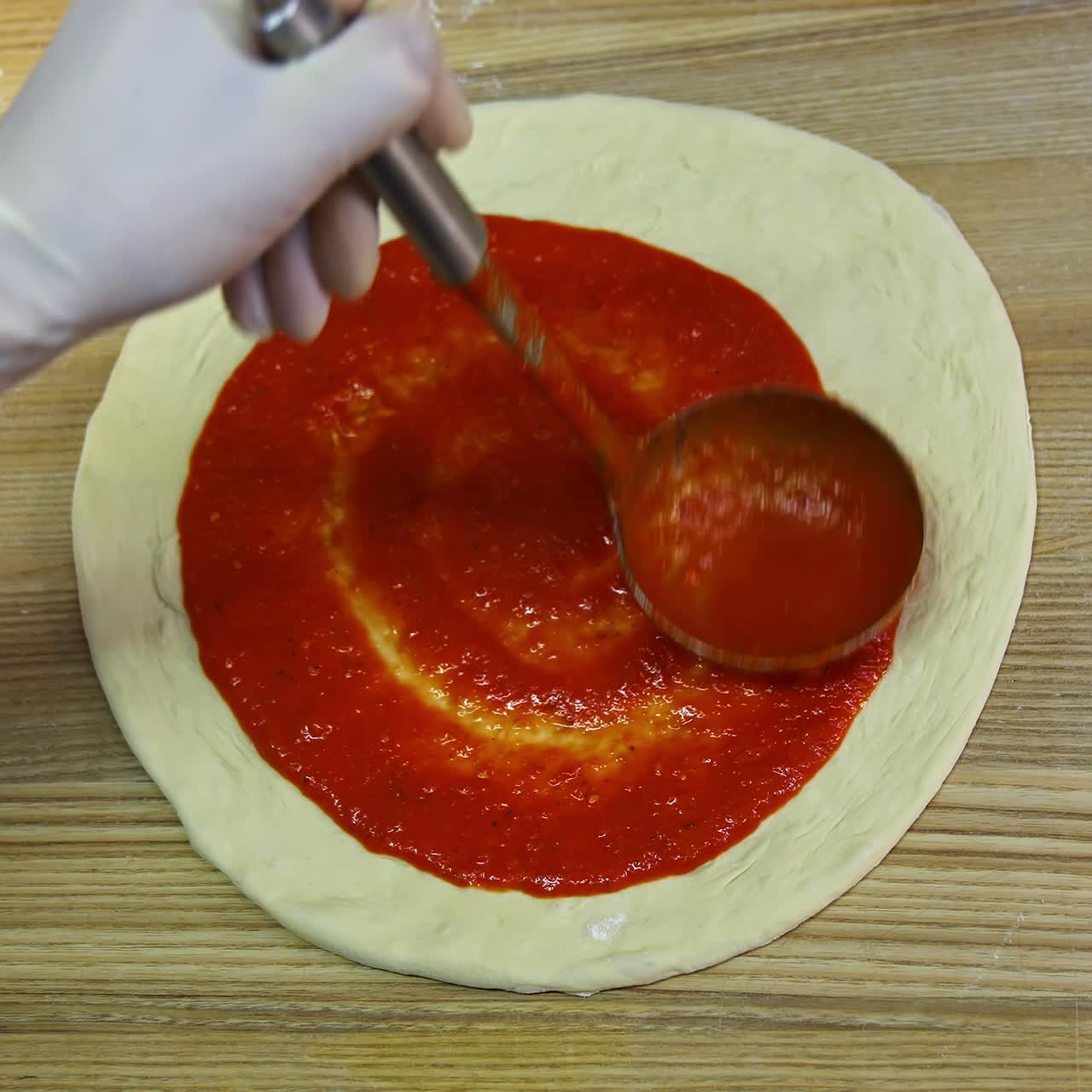 Chef che spalma salsa di pomodoro sull'impasto della pizza con un mestolo. Ristorante pizzeria tradizionale. Filmato di cibo. Primo piano