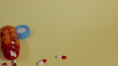 slow motion high-angle medium shot as a bottle full of pills falls vertically, bounces, looses the lid and spills pills