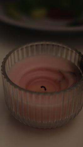 vela aromática rosada decorativa soplada en un soporte de vidrio cerca de un vaso de vino en una mesa de luz con un entorno festivo en una habitación semidescura en primer plano en cámara lenta
