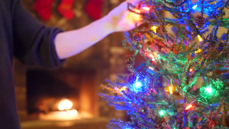 Decorating-a-christmas-tree-with-colorful-festive-lights,-ornaments-and-stockings-over-the-fireplace-during-the-holidays