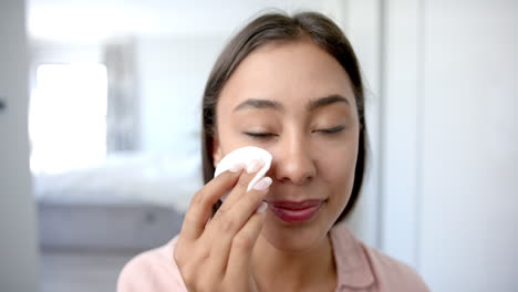 applying makeup remover, woman cleaning face with cotton pad at home