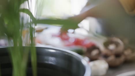 Midsection-of-african-american-woman-in-apron-chopping-vegetables-in-kitchen,-rack-focus-slow-motion