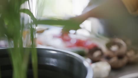 sección media de una mujer afroamericana en un delantal cortando verduras en la cocina, enfoque en el estante en cámara lenta