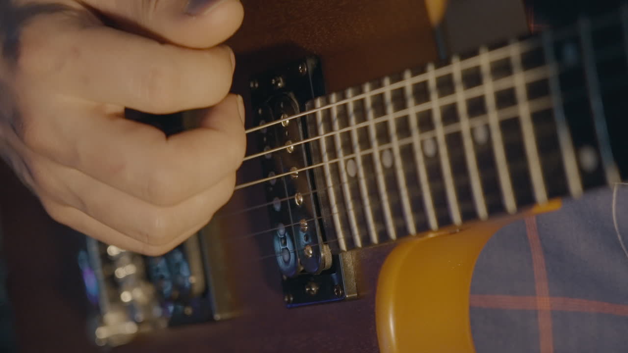 Primo piano di una mano che strimpella le corde di una chitarra elettrica