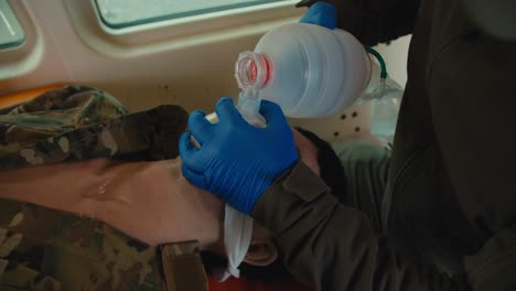 close-up of a confident male medic in a dark green army uniform and blue gloves performing artificial respiration using a male soldier doll during first aid training in the ambulance cabin