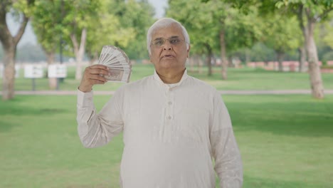 indian old man using money as fan in park