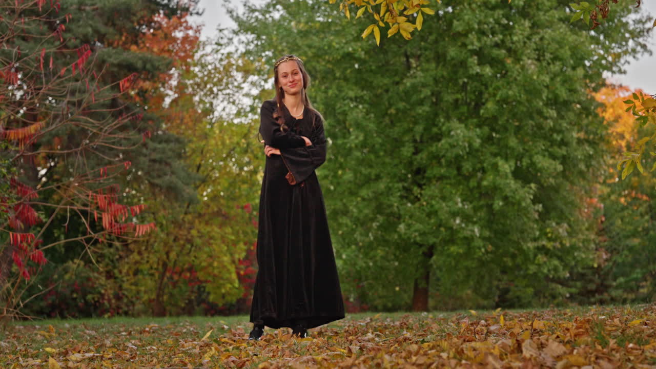 Cinematic dolly left shot of a medieval woman in black velvet smiling among red and golden autumn leaves in a natural forest with warm moody light