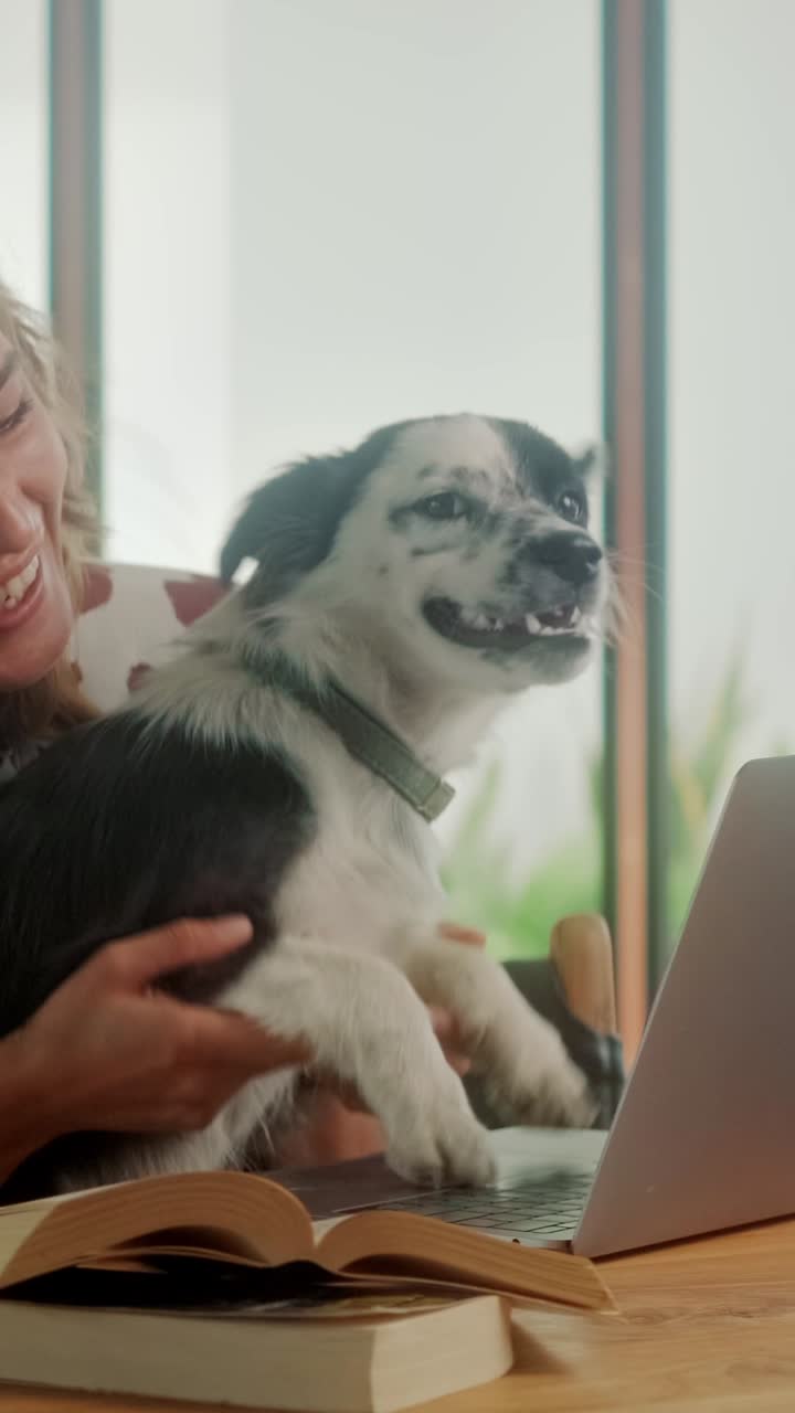 Woman interacts with dog while working on laptop indoors