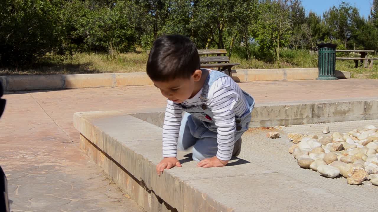 可愛兩歲男童在公園裡玩石頭。