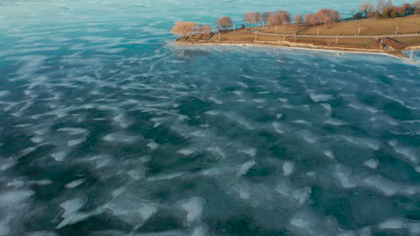 Aerial-shot-of-park-land-by-frozen-icy-blue-river