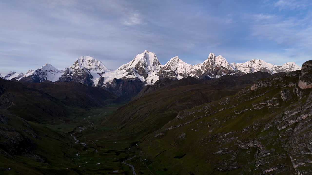Cinematic aerial view of snowy Andes mountains in Peru with glaciers, rocky cliffs, and hidden blue alpine lake under misty clouds, dramatic landscape and natural travel destination