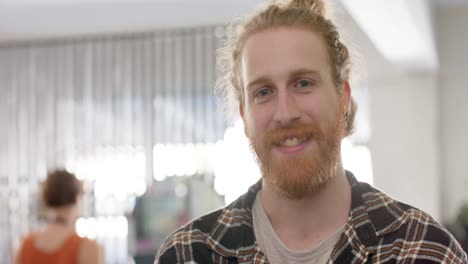 Portrait-of-bearded-caucasian-male-hairdresser-in-apron-smiling-at-hair-salon,-slow-motion