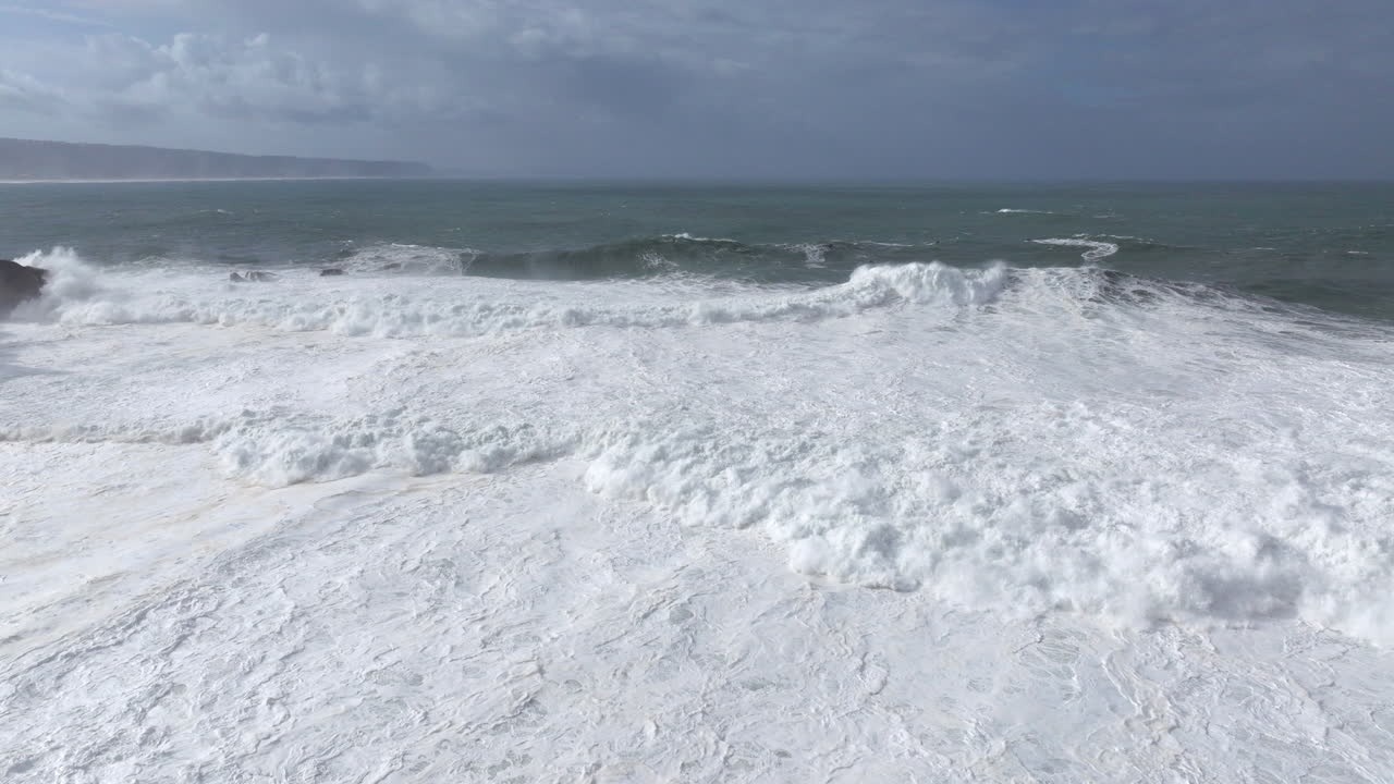 Aerial drone shot of big waves coming into shore on a day with giant waves in Nazaré, Portugal, Europe. Jet ski riders and surfers in Atlantic Ocean. Big wave surfing town