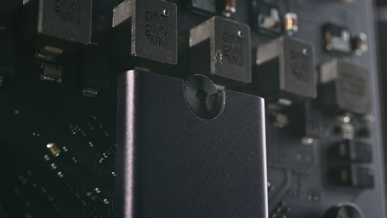 Macro shot inside a dark aluminium computer, low angle of SSD solid-state drive, motherboard, capacitors and components. Dramatic lighting, metallic, matten modern, reflective interior hardware