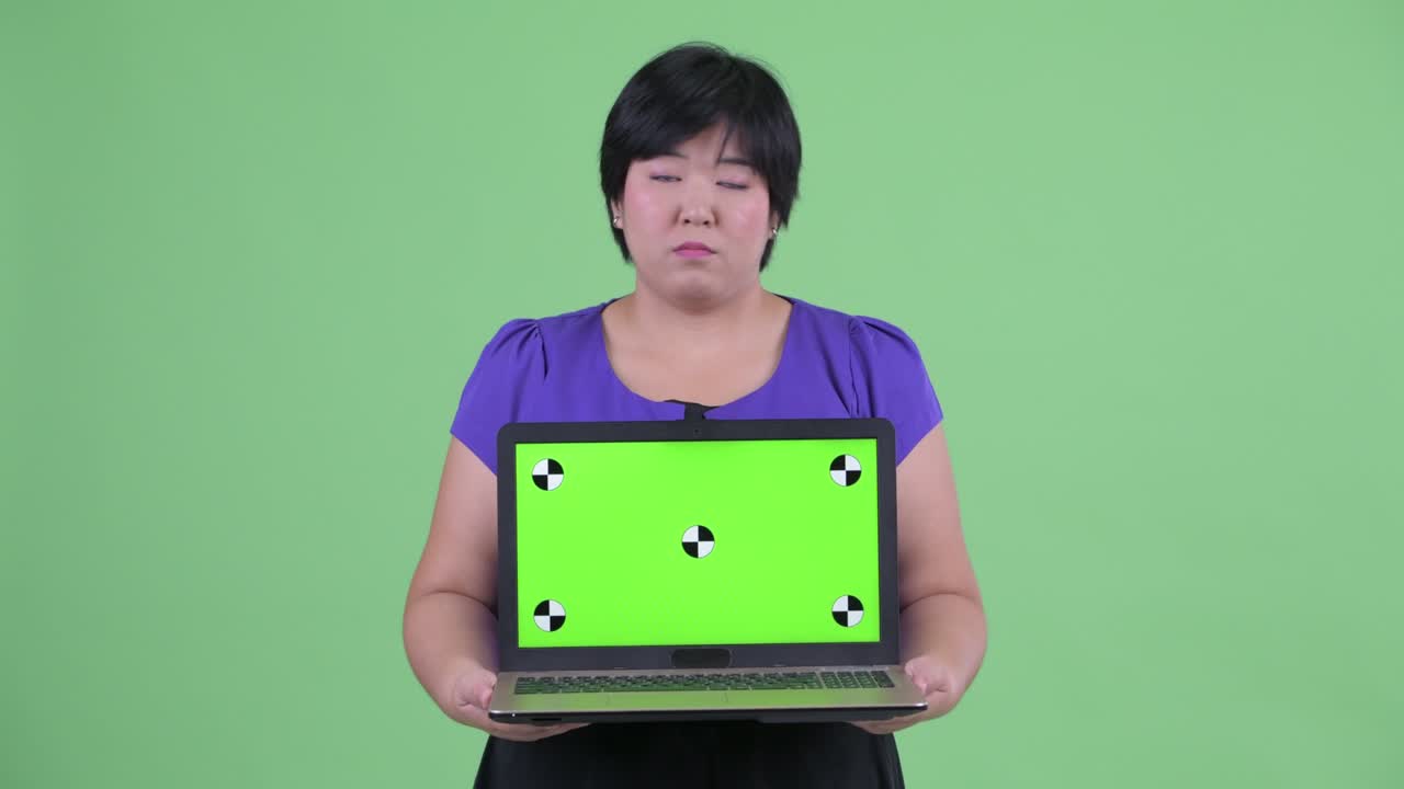 초록색 배경에 슬프게 보이는 노트북에서 크로마 키를 보여주는 짧은 헤어 스타일의 과체중 아시아 여성의 초상화