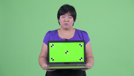 portrait of overweight asian woman with short hairstyle showing chroma key from laptop while looking sad against green background