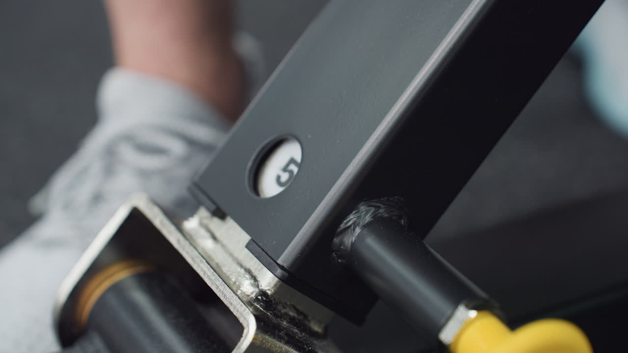Fitness enthusiast adjusts bench angle by pulling adjustment knob on leg press machine before intense workout, showing hand detail, metal frame, seat pad and gear in modern interior close up shot