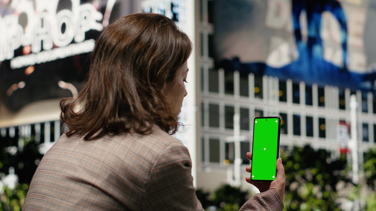 Smartphone con schermo verde usato da una donna d'affari seduta su una panchina del parco.
