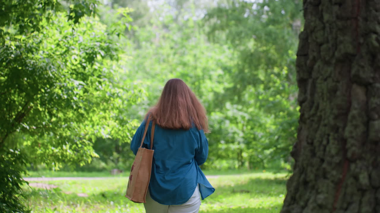 Elegant lady wearing sunglasses and casual outfit turns around in green park surrounded by trees and sunlight, preparing to walk away with calm confident expression under warm summer light breeze