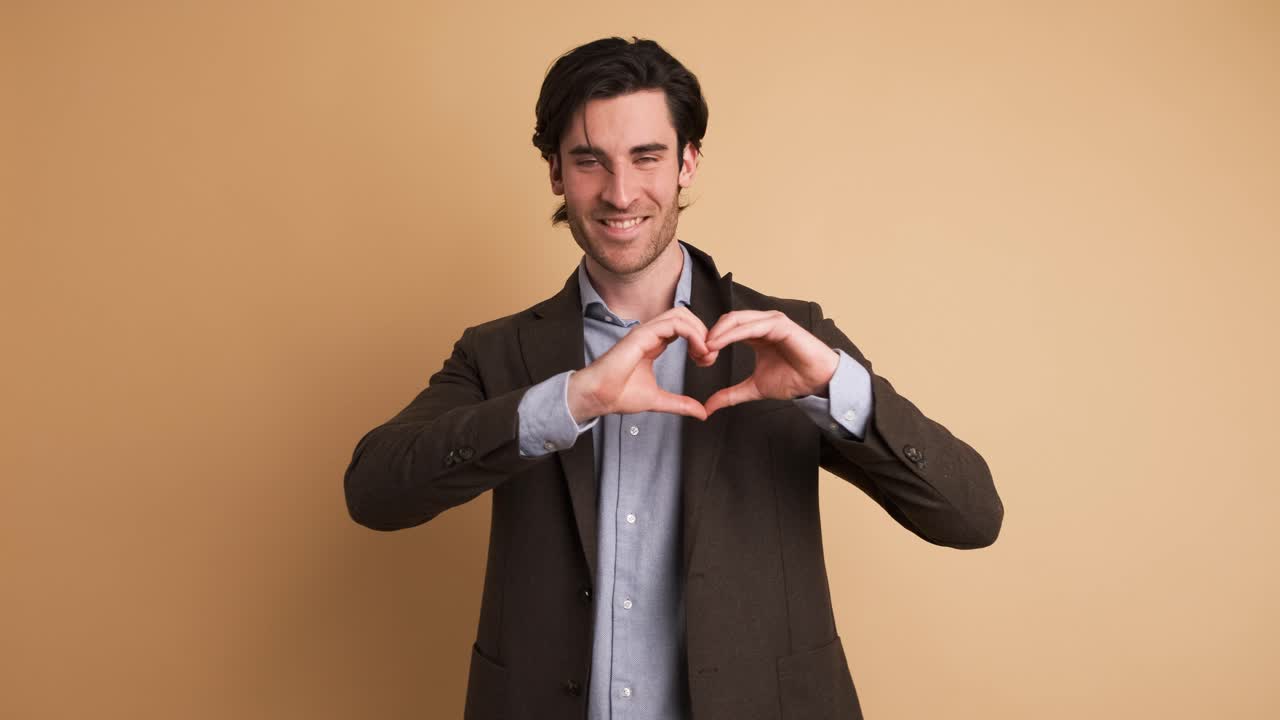 Happy businessman gesturing heart on brown background
