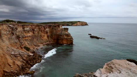 a long pan of a rocky coast into a cliff made of orange and red rocks layered from years of erosion