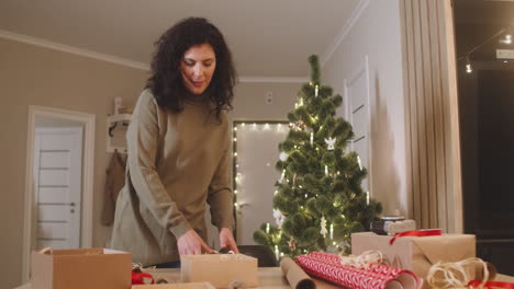 mujer morena envolviendo regalos de navidad en una mesa en una habitación decorada con un árbol de navidad 1