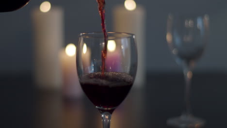 red wine being poured in glass with candles lit in background