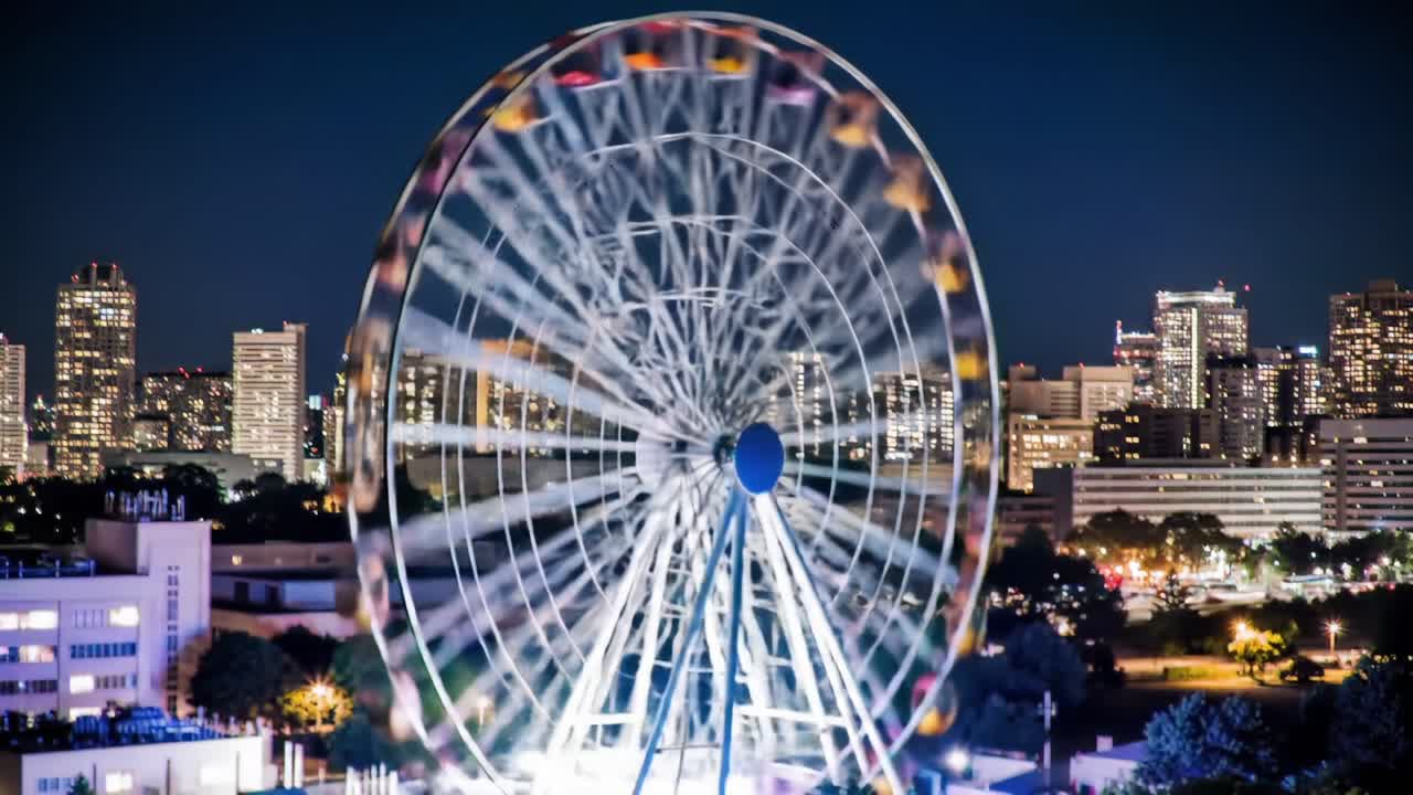 A Vibrant Ferris Wheel Illuminated Against a Night Sky, Showcasing Colorful Baskets and a Stunning City Skyline in the Background, Perfect for Capturing Evening Festivities
