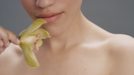 close up portrait beauty woman touching skin with orchid flower caressing smooth healthy complexion enjoying natural sensual fragrance flirtatious young female on grey background skincare concept