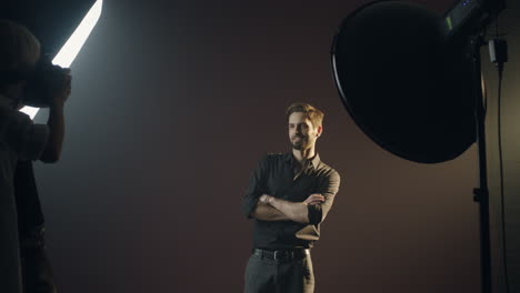 young caucasian man model posing in dark studio while the photographer taking shots of him