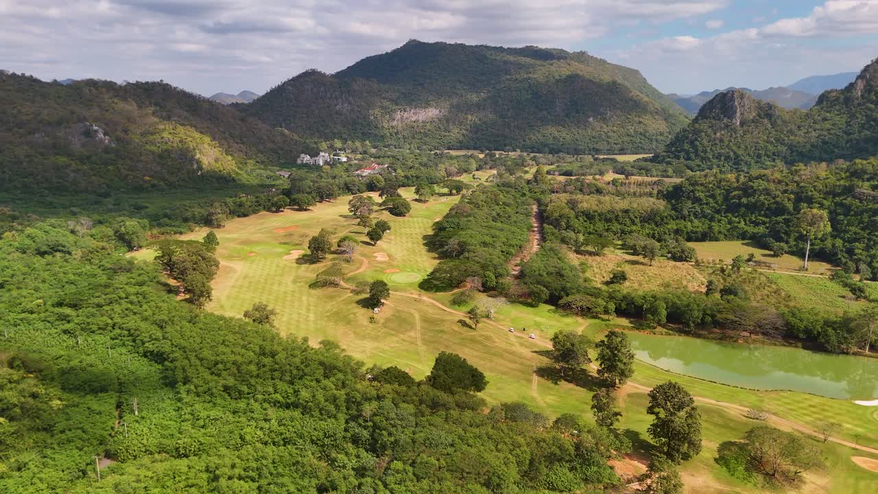 Sebuah drone terbang di atas lapangan golf indah yang dikelilingi oleh pegunungan kapur dan hutan tropis