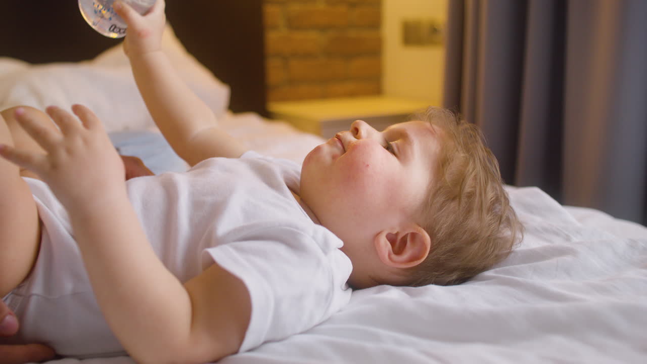 젖병에서 물을 마시면서 침실에 있는 침대에 누워 있는 아기의 모습을 가까이서 볼 수 있습니다.